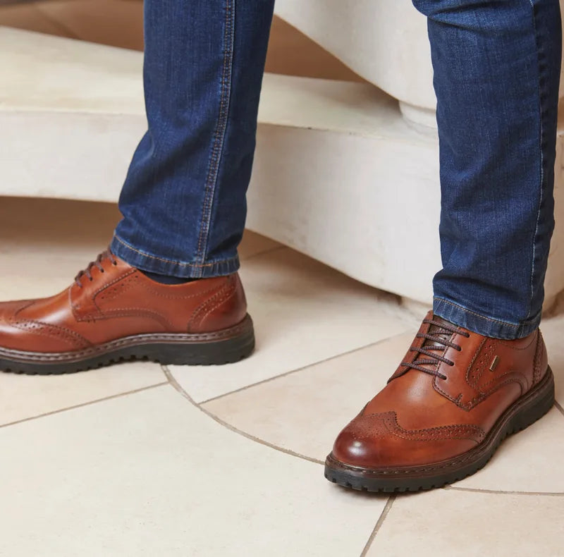 Josef Seibel Erroll 59 Brown mens smart leather shoe. Experience unparalleled style and comfort with this smart casual shoe. Crafted from premium leather, it effortlessly combines durability and support with a durable sole for superior grip. Colour: Brown Material: Leather Brown leather shoes worn with blue jeans on a tiled floor.