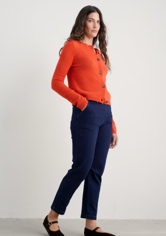 Woman wearing an orange sweater and navy pants on a white background
