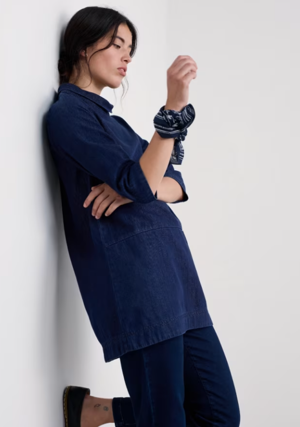 Seasalt Curlew Cry Denim Tunic Mid Wash womens tunic that is Easy-fit A-line shape with Cowl neck and Dropped waist and Patch pocket that is Machine Washable Woman wearing a navy blue shirt and pants against a white background