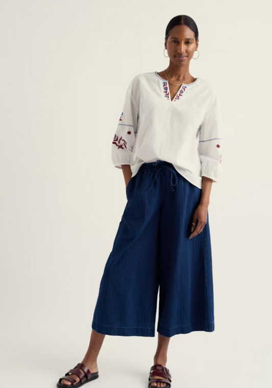 Seasalt Eskelli Wide Leg Culotte Mid Wash womens Wide leg with Elasticated waist band and a Drawstring tie fastening that has Back pockets and Side pockets that can be Machine Wash 30C Colour: Mid Wash Material: 100% Linen Woman wearing a white embroidered blouse and blue pants on a white background