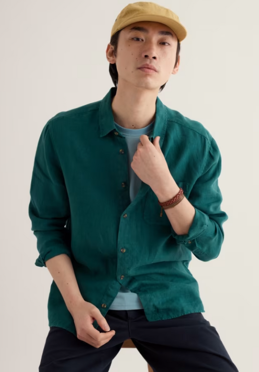 Seasalt Men's Curator Linen Shirt Grasshopper Material: 100% Linen Crafted from breathable linen, the Seasalt Men's Curator Shirt in Grasshopper green is your go-to relaxed-fit summer essential features a classic collar and long sleeves, perfect for casual days or seaside escapes. The natural fabric keeps you cool and comfortable, while the understated green hue pairs effortlessly with shorts, chinos, or linen trousers. LightweigMan wearing a green shirt, beige cap, and dark pants against a plain background