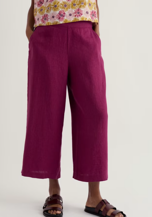 Seasalt Merrivale Linen Culottes Dark Freesia Material: 100% Linen these womens Culottes offer effortless summer style with breathable linen construction. The relaxed culotte silhouette provides comfortable, flattering coverage perfect for spring/summer weather dressing. Rich purple tones complement any seasonal wardrobe. Ideal for casual outings, garden gatherings, or leisurely days when you want to stay cool without compromising on style. Person wearing magenta wide-leg pants with a white background