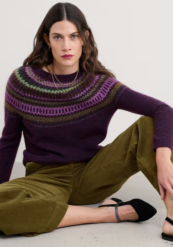 Seasalt Annik Fair Isle Jumper Modernist Grape Oak Mix seasalt clothing womens striped warm jumper Woman wearing a purple and green patterned sweater sitting on the floor.