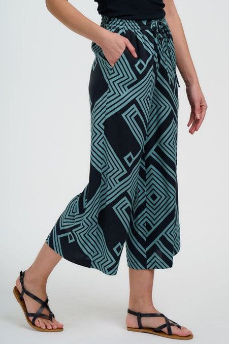 Sugarhill Clothing Brighton Ameera Cropped Wide Leg Trousers Black/Green Geometric Lines. Womens Cropped Wide leg, Elasticated waistband drawstring tie, Pockets and Machine washable (delicate) Material: 100% Lenzing Ecovero Viscose. Sugarhill Brighton's Ameera trousers bring effortless style to your wardrobe. Cut from luxuriously soft Lenzing viscose, these cropped wide-leg trousers feature a striking black and green geometric line pattern tPerson wearing teal and black patterned pants on a white background