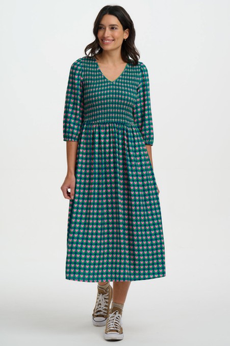 Sugarhill Brighton Della Shirred Midi Dress Navy Heart Tile womens Midi length with Pockets that's Machine Washable (Delicate) Colour: Navy Heart Tile Material: 100% Viscose Description: The Della Shirred Midi Dress Woman wearing a green checkered dress on a white background