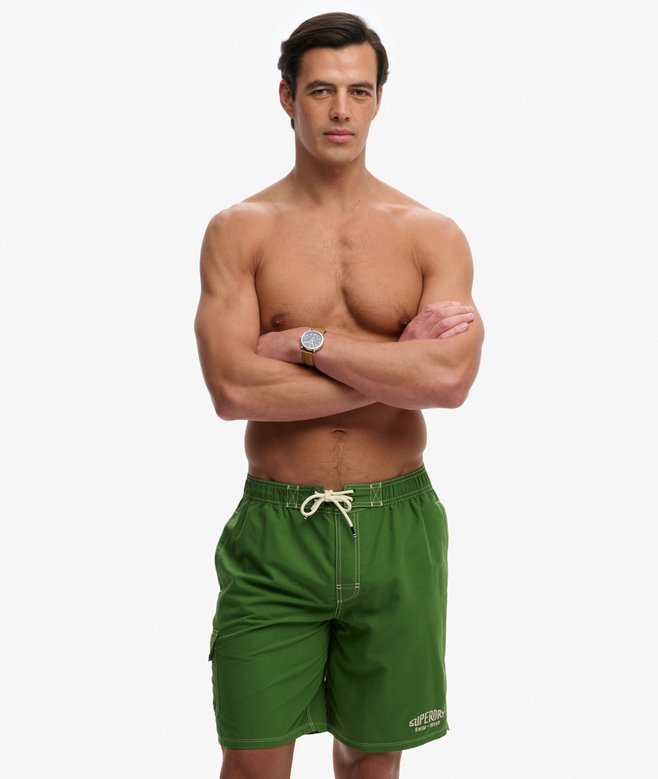 Superdry Cargo 19-Inch Boardshorts Banana Palm Green mens shorts that are Relaxed fit  with a Lower rise with an internal mesh lining and Two external side pockets with mesh lining with Side pocket on thigh with hook and loop fastening and embroidered badge and Elasticated drawstring waist with hook and loop fastening and Embroidered Superdry logo on thigh and embroidered badge and elasticated waist Colour: Banana Palm Green Material: 100% Recycled Polyester wearing green swim shorts on a white background