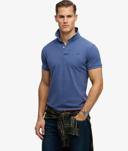 Superdry Classic Pique Polo Shirt Bay Blue mens Relaxed fit – the classic Superdry fit. Not too slim not too loose just right. Go for your normal size. with a Crafted from a pique fabric with a regular collar and two-button fastening that's Ribbed trims on the sleeves and split side seams Colour: Rich Burgundy Material: 100% Organic Cotton Man wearing a blue polo shirt with a white background