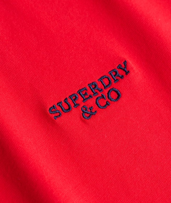 A close-up of a bright red fabric surface with dark navy embroidered text reading 'SUPERDRY & CO'.