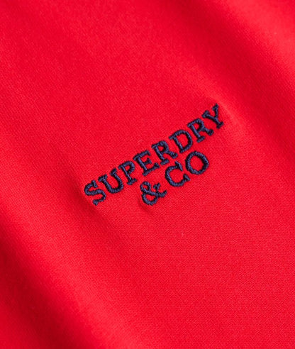 A close-up of a bright red fabric surface with dark navy embroidered text reading 'SUPERDRY & CO'.