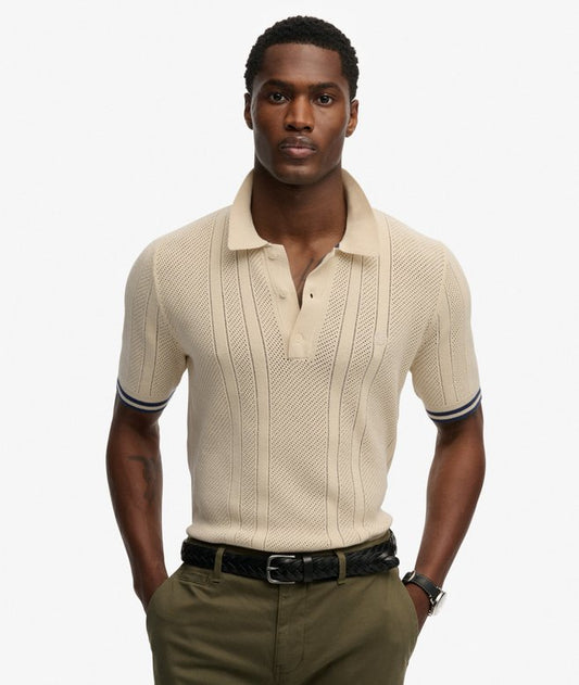 Superdry Knitted Texture Short Sleeve Polo Shirt Oatmeal Beige mens Relaxed fit the classic Superdry fit. Not too slim not too loose just right. Go for your normal size with Single collar with button fastening that's Ribbed trims with contrasting cuffs Colour: Oatmeal Beige Material: 100% Organic Cotton Man wearing a beige knitted polo shirt and green pants on a white background