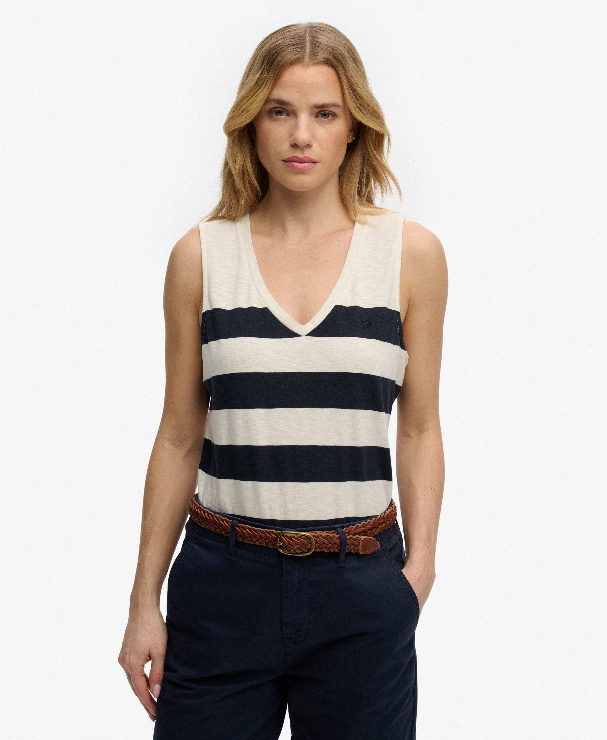 Superdry Studios V-Neckline Vest Top Off White/Navy Wide Stripe womens top that's Relaxed fit with a V-Neckline and Embroidered logo on the chest Colour: Off White/Navy Wide Stripe Material: 60% Cotton & 40% Lyocell Woman wearing a striped tank top and dark pants on a white background