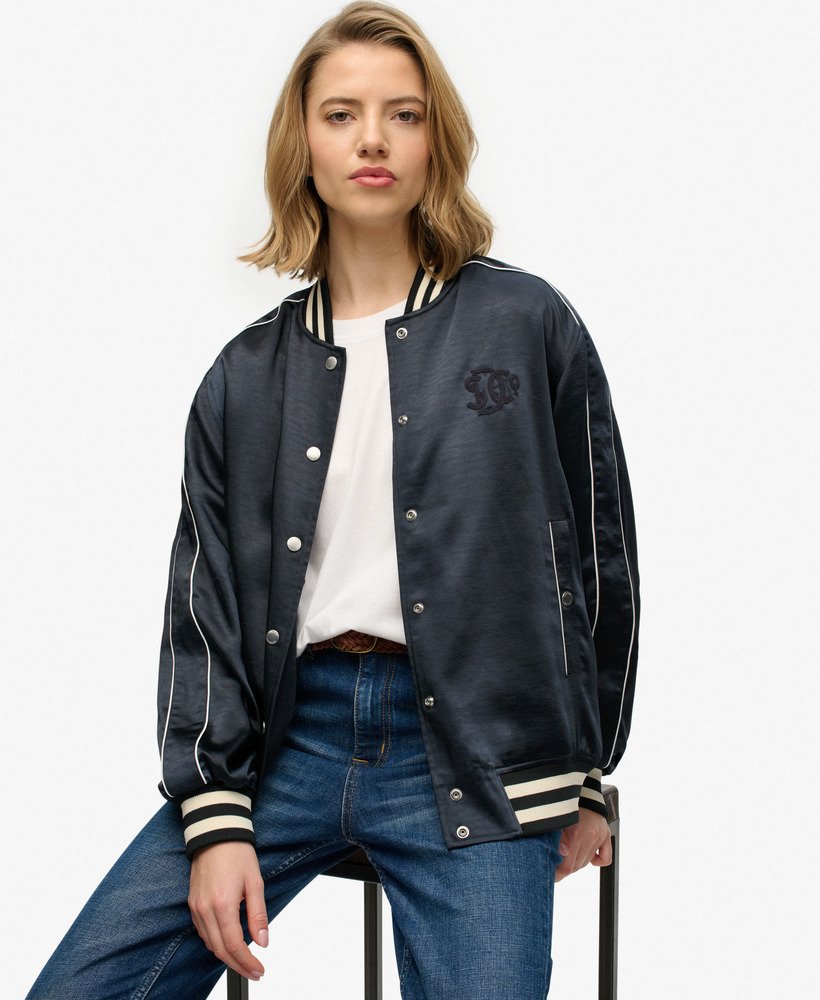 Superdry Varsity Satin Bomber Jacket Eclipse Navy womens Slim fit with Popper fastening and Ribbed hem cuffs and collar that's Two popper fastened pockets and has Embroidered text on chest and back of neckline 100% Recycled Polyester Person wearing a navy varsity jacket with white accents on a white background