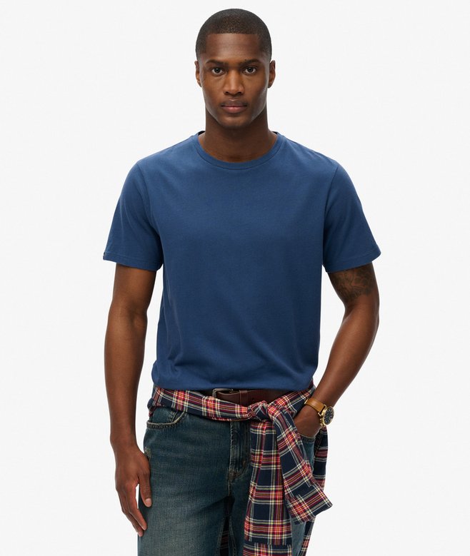Superdry Classic Essential T-Shirt Skate Navy Mens Tshirt Superdry Clothing Buy 3 Essential Logo T-Shirts For £50 Man wearing a blue t-shirt and plaid shirt over jeans on a white background