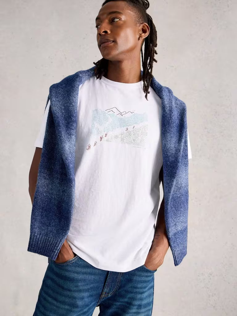 White Stuff Abersoch Pedal Graphic Tee White mens t-shirt Crew Neck that's Short Sleeve and Regular Fit that's Machine Washable Colour: White Material: 100% Cotton Person wearing a white t-shirt with a graphic design, blue sweater, and jeans against a plain background