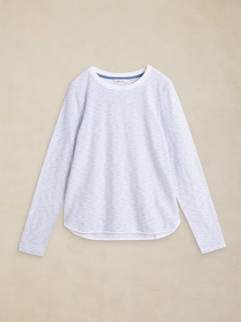 A white long-sleeve crewneck top with thin blue horizontal stripes, laid flat on a textured beige background.