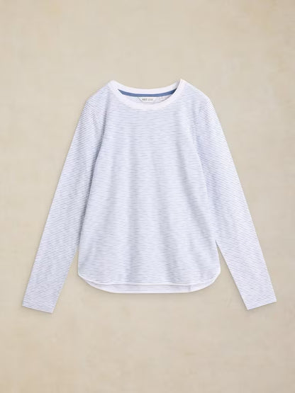 A white long-sleeve crewneck top with thin blue horizontal stripes, laid flat on a textured beige background.