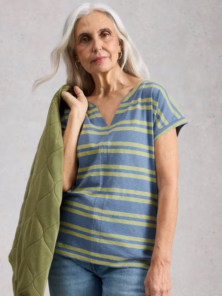 White Stuff Nelly Notch Stripe Tee Blue Multi womens Buy 2 Selected T-Shirts For £45 Notch Neck with Short Sleeve and a Regular Fit that's Machine Washable Colour: Blue Multi Material: 100% Cotton Style Code: 445350 Woman wearing a blue and yellow striped shirt with a green jacket over her shoulder against a plain background