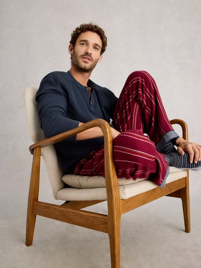 White Stuff Helston Waffle Henley Dark Navy Mens Long Sleeved Tshirt White Stuff Man sitting in a wooden chair wearing a dark blue shirt and red plaid pants.