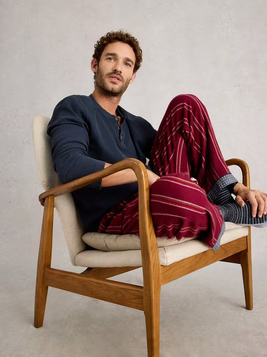 White Stuff Helston Waffle Henley Dark Navy Mens Long Sleeved Tshirt White Stuff Man sitting in a wooden chair wearing a dark blue shirt and red plaid pants.
