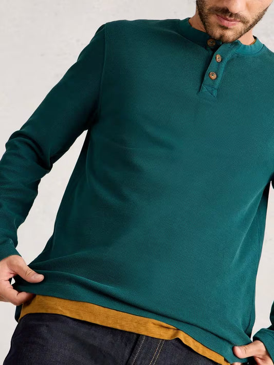 White Stuff Helston Waffle Henley Mid Green Man wearing a teal long-sleeve shirt with brown trim against a light gray background