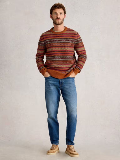 White Stuff Ossett Fairisle Crew Neck Orange Mens Jumper White Stuff Clothing Man wearing a patterned sweater and blue jeans against a plain background